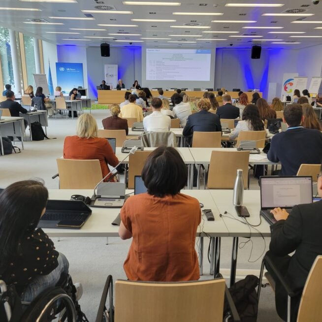 Participants at a workshop in Bonn sit behind desks and look towards a slide show projected at the front of the room.